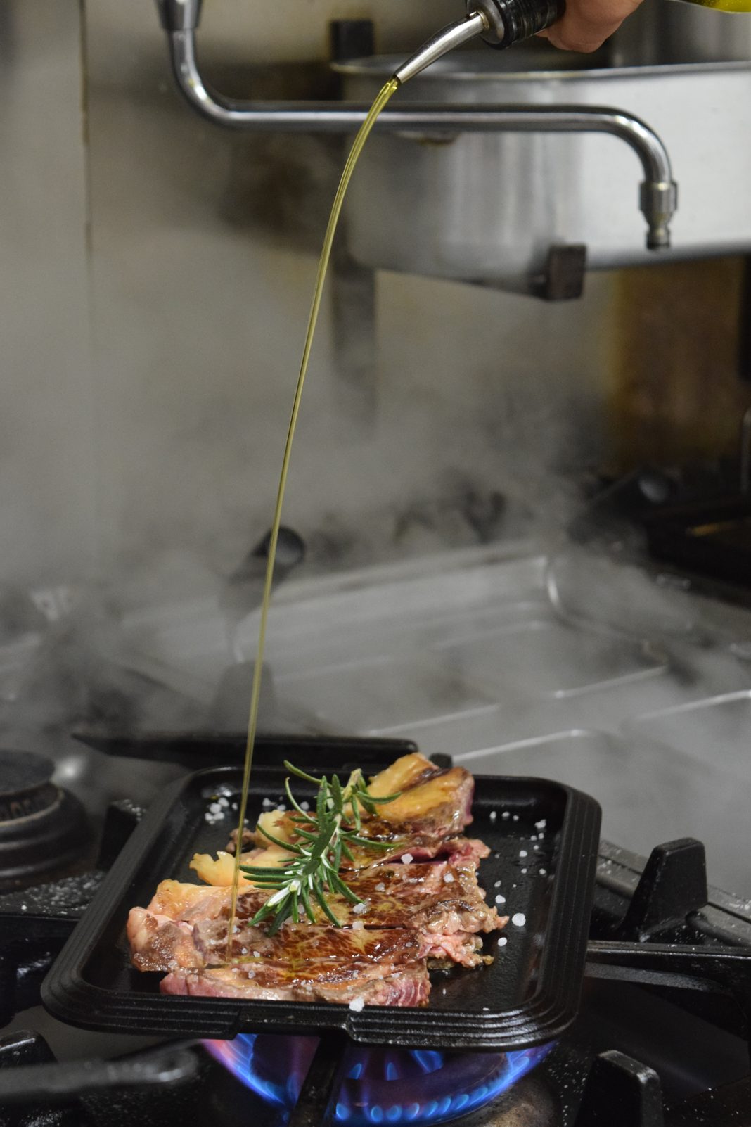 Olio versato sulla carne alla piastra con il rosmarino